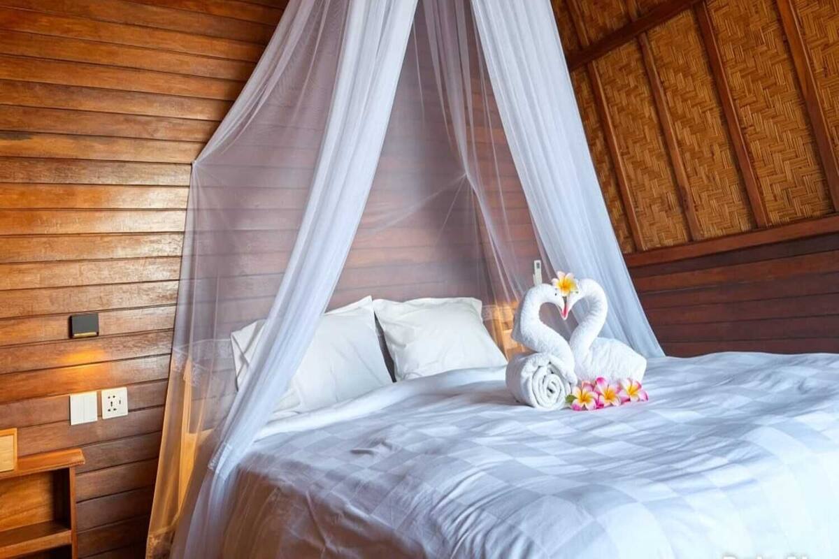 A room with a bed, white canopy, and a decorative swan towel arrangement.
