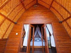 A wooden room with a bed, a window with curtains, and a view of the outdoors. - Cozzy Sea Dream Cliff Eco Guest House (Penida Island)