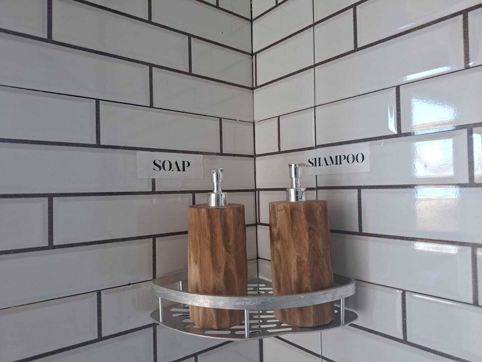 A bathroom corner with white tiles and two wooden dispensers labeled 'SOAP' and 'SHAMPOO'.