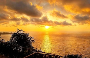 A sunset over a body of water with a railing in the foreground. - Cozzy Sea Dream Cliff Eco Guest House (Penida Island)