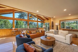 A spacious living room with large windows, a wooden ceiling, and a mix of sofas and chairs. - View Cabin - Mountain Retreat w/ Hot Tub + Sauna (Springville)