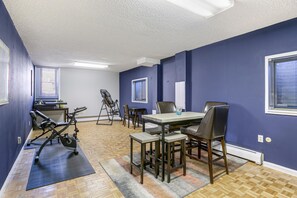 Ein Zimmer mit Esstisch, Stühlen, Laufband und Fitnessgeräten.
