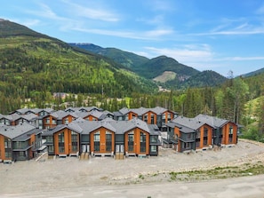Une rangée de chalets modernes à plusieurs étages, dotés de grandes fenêtres, se dressant sur un fond de montagnes boisées.