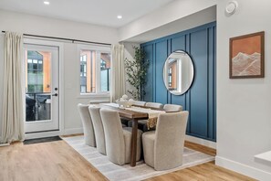 Un coin repas comprenant une table, des chaises, un miroir et une vue sur l’extérieur, visible à travers une porte vitrée.