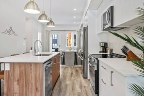 A modern kitchen with a central island, stainless steel appliances, pendant lighting, and a view into the dining area. - Ridgeline | Slope-Side | Hot Tub | Resort Access (Panorama)