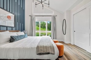 Une chambre moderne avec un grand lit, une vue sur la verdure par la fenêtre et un décor minimaliste.