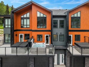 Un immeuble moderne à plusieurs étages, doté de grandes fenêtres, d’un jacuzzi sur le toit et d’un espace extérieur couvert.