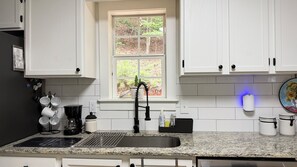 A kitchen with white cabinets, a granite countertop, a black faucet, and a window with a view of trees.