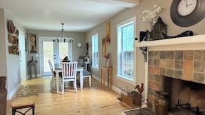 A spacious room with a fireplace, wooden flooring, and a dining area with chairs and a table.