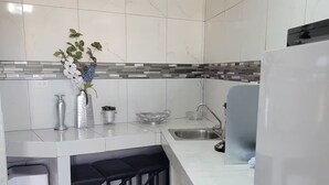 Una cucina moderna con mobili bianchi, schienale rivestito di piastrelle, lavello in acciaio inossidabile e frigorifero integrato.