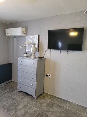 A room with a grey dresser, a mounted flat-screen TV, and a white radiator. - Happy Place (Santa Ana)
