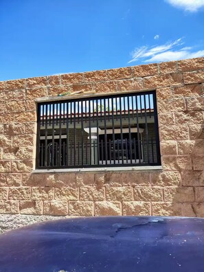 A stone building with a barred window and a car parked in front. - Happy Place (Santa Ana)