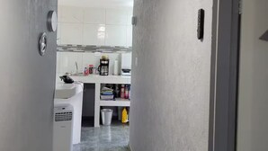 Un corridoio stretto che conduce a una cucina, con una ventola a soffitto, una lavatrice e un cestino.