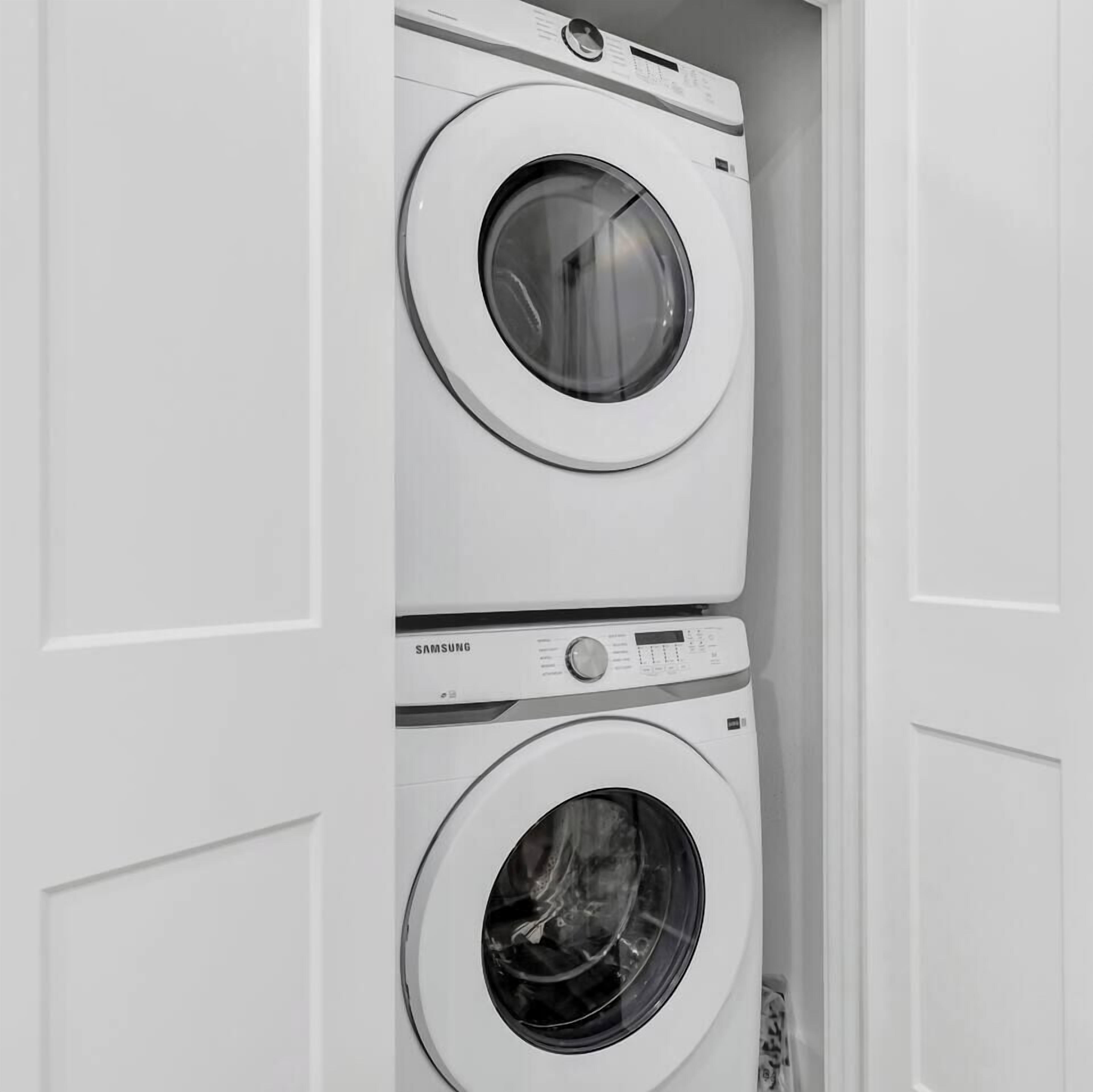 Uma máquina de lavar e secar empilhadas num quarto com paredes brancas.