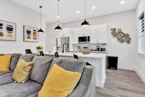 A modern living room with a gray sofa, yellow cushions, and a coffee bar in the background. - Dallas Escape w/ Rooftop + Yard • Sleeps 10 (Dallas)