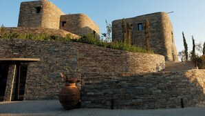 A stone building with a circular tower, a large potted plant, and a paved entrance. - KHAI SYVOTA (Igoumenitsa)
