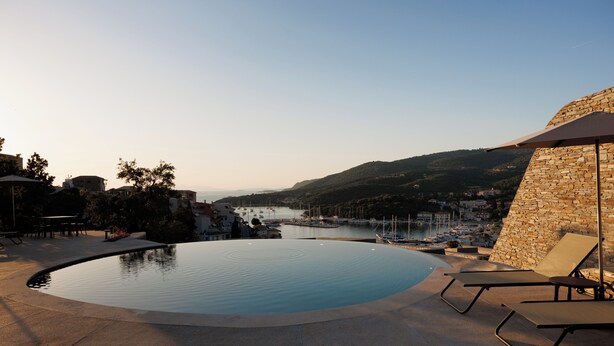 A swimming pool with lounge chairs, a stone wall, and a view of a marina and hills. - KHAI SYVOTA (Igoumenitsa)