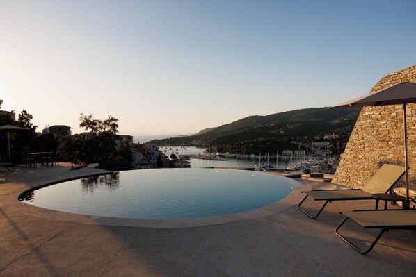 A swimming pool with lounge chairs, a stone wall, and a view of a marina and hills.