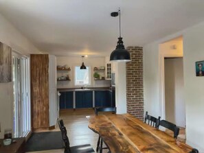 A dining area with a long wooden table, black chairs, and a hanging pendant light.
