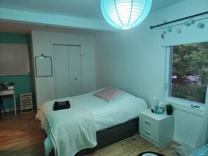 A bedroom with a bed, bedside table, window, and a desk with a chair.