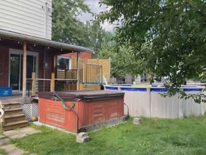 A backyard with a wooden deck, a hot tub, a swimming pool, and a fenced area.