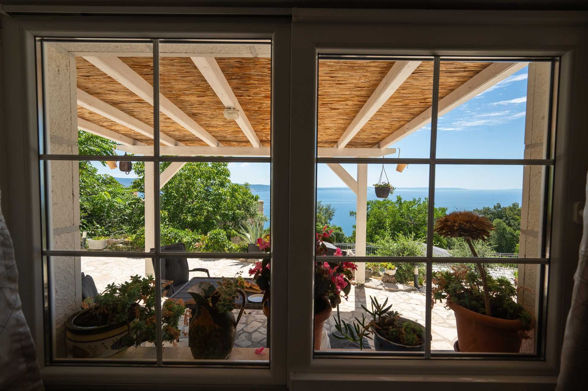 A window with a view of a patio area with potted plants and a clear sky.