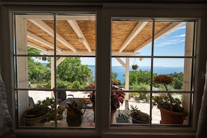 A window with a view of a patio area with potted plants and a clear sky. - Villa Ole | Mediterranean Stone Villa with Pool, Jacuzzi (Jesenice)