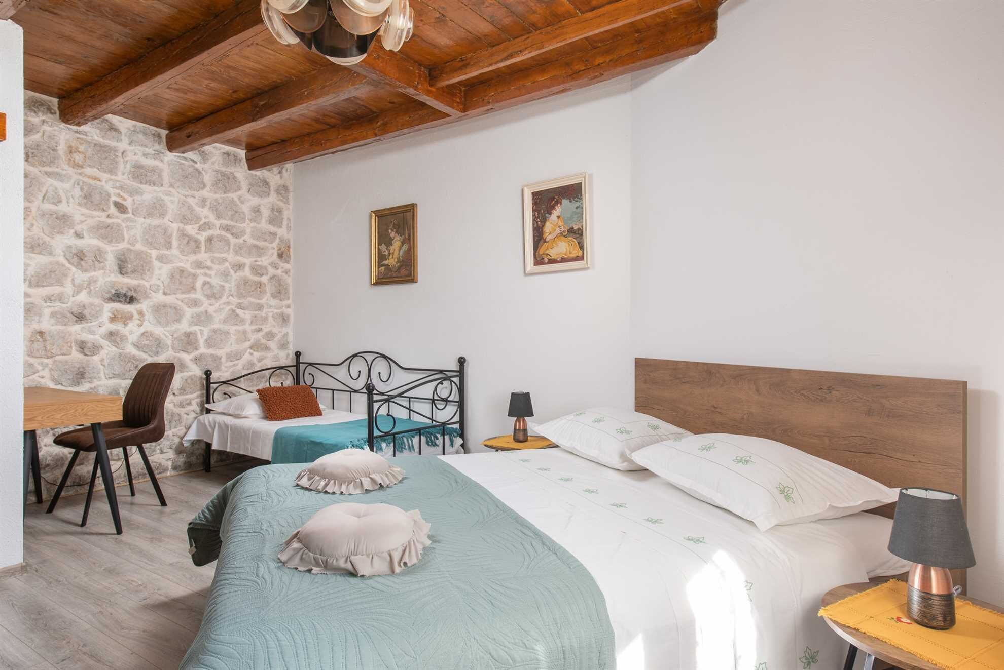 Ein Schlafzimmer mit Steinwand, einem Bett mit Holz Kopfteil, einem Schreibtisch mit Stuhl und zwei gerahmten Bildern an der Wand.