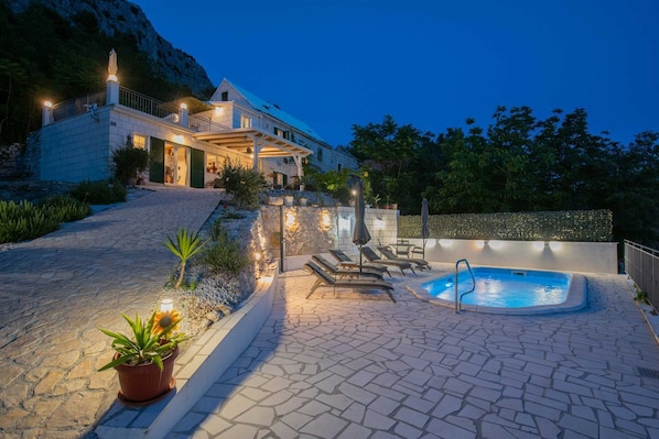 A pool area with lounge chairs, a hot tub, and a stone pathway leading to a building. - Villa Ole | Mediterranean Stone Villa with Pool, Jacuzzi (Jesenice)