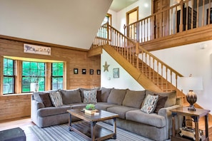 Ein geräumiges Wohnzimmer mit einer großen Eckcouch, einer Holztreppe und Blick ins Freie.