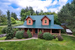 Eine Blockhütte mit einem grünen Metalldach, einer Veranda und einem Steinpfad, der zum Eingang führt.