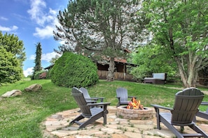 Eine Terrasse mit Adirondack-Stühlen und einem Feuerkorb, umgeben von einem Kiesweg und üppigem Grün.