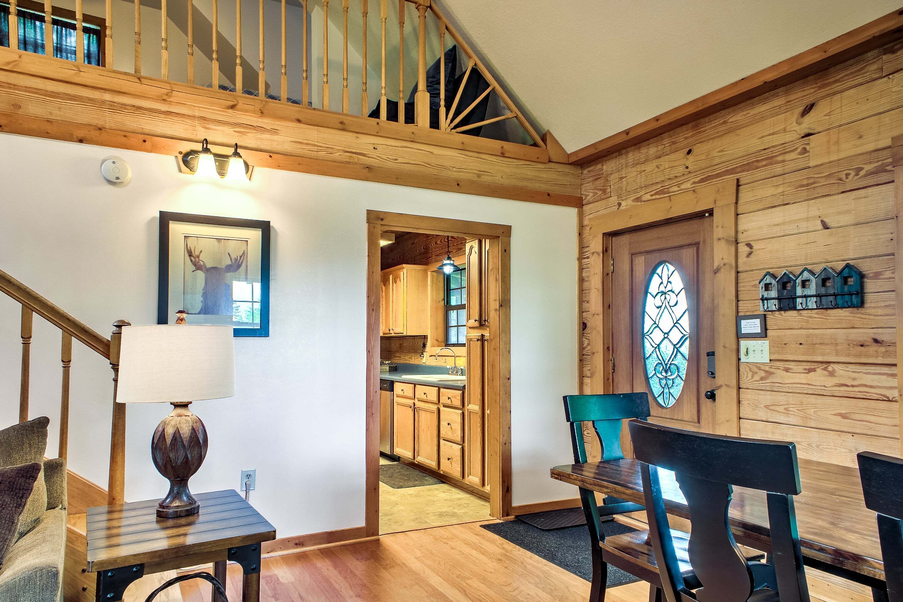 A wooden staircase, a dining area with chairs, a table, a lamp, and a kitchen visible through an open door.