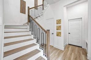 Eine Treppe mit Holzstufen, schwarzen Geländern, weißen Wänden und einer Tür mit drei goldenen Zierteilen.