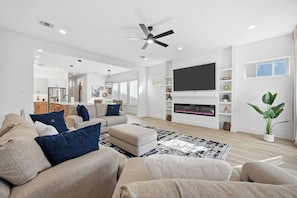 Ein modernes Wohnzimmer mit Sofa, Hocker, Kamin, Fernseher, Deckenventilator und einer Topfpflanze.