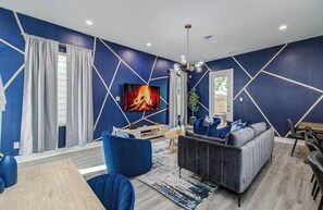 Ein modernes Wohnzimmer mit blauem geometrischen Wanddesign, einem Kamin, einer Couch und einem Fernseher.