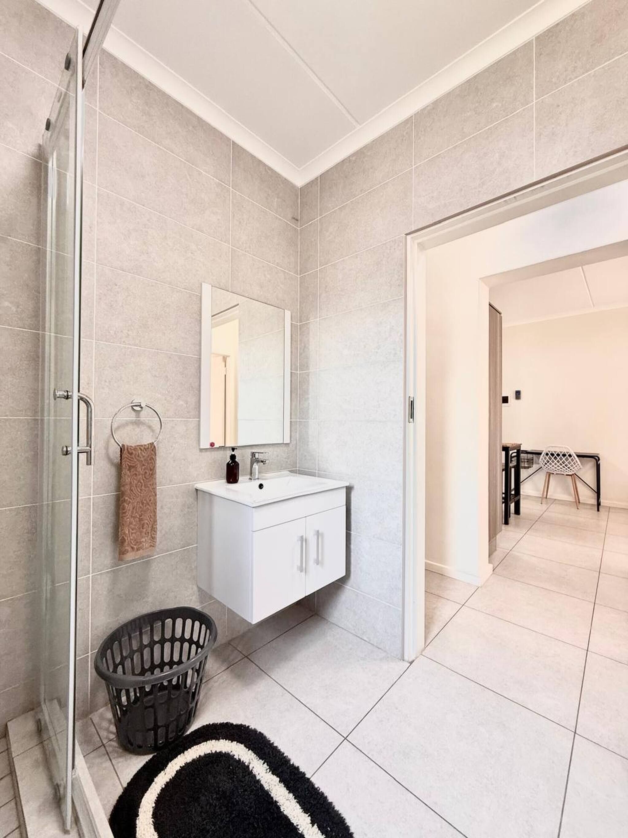 Un baño moderno con cabina de ducha de vidrio, un tocador blanco con espejo y una alfombra blanco y negro en el suelo.