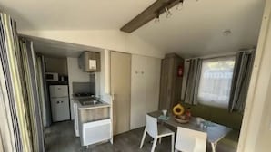Une cuisine compacte équipée d’un évier, d’une cuisinière et d’un four à micro-ondes, un coin repas avec une table et des chaises, et une vue sur l’extérieur à travers une fenêtre avec des rideaux.
