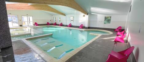 Piscina com várias pistas, rodeada por cadeiras cor-de-rosa e um chão em mosaico.