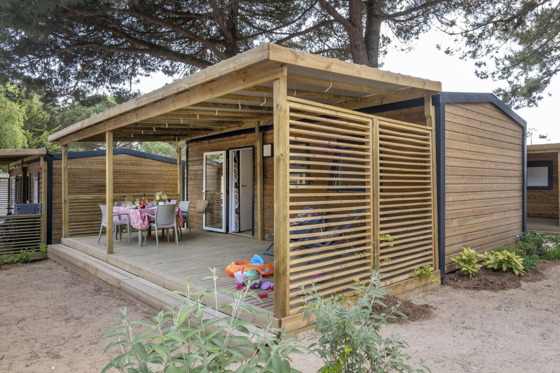 Una estructura de madera con un patio cubierto, una mesa con sillas y un pequeño jardín.