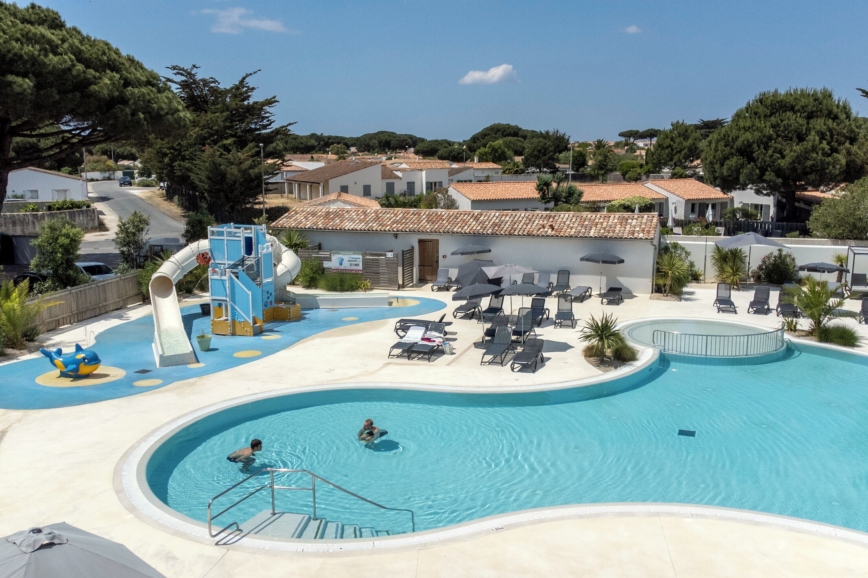 Une piscine avec un toboggan, des chaises longues et un petit espace piscine.