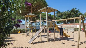 Ein Spielplatz mit Rutsche, Kletternetz und Schaukeln.