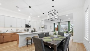 Une cuisine moderne avec des meubles blancs, un îlot central et un coin repas comprenant une table en bois et des chaises grises.