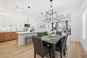 Eine moderne Küche mit weißen Schränken, einer zentralen Kochinsel und einem Essbereich mit Holztisch und grauen Stühlen.