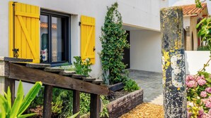 Un cortile con un pavimento in legno, un edificio bianco con persiane gialle e una colonna con graffiti.