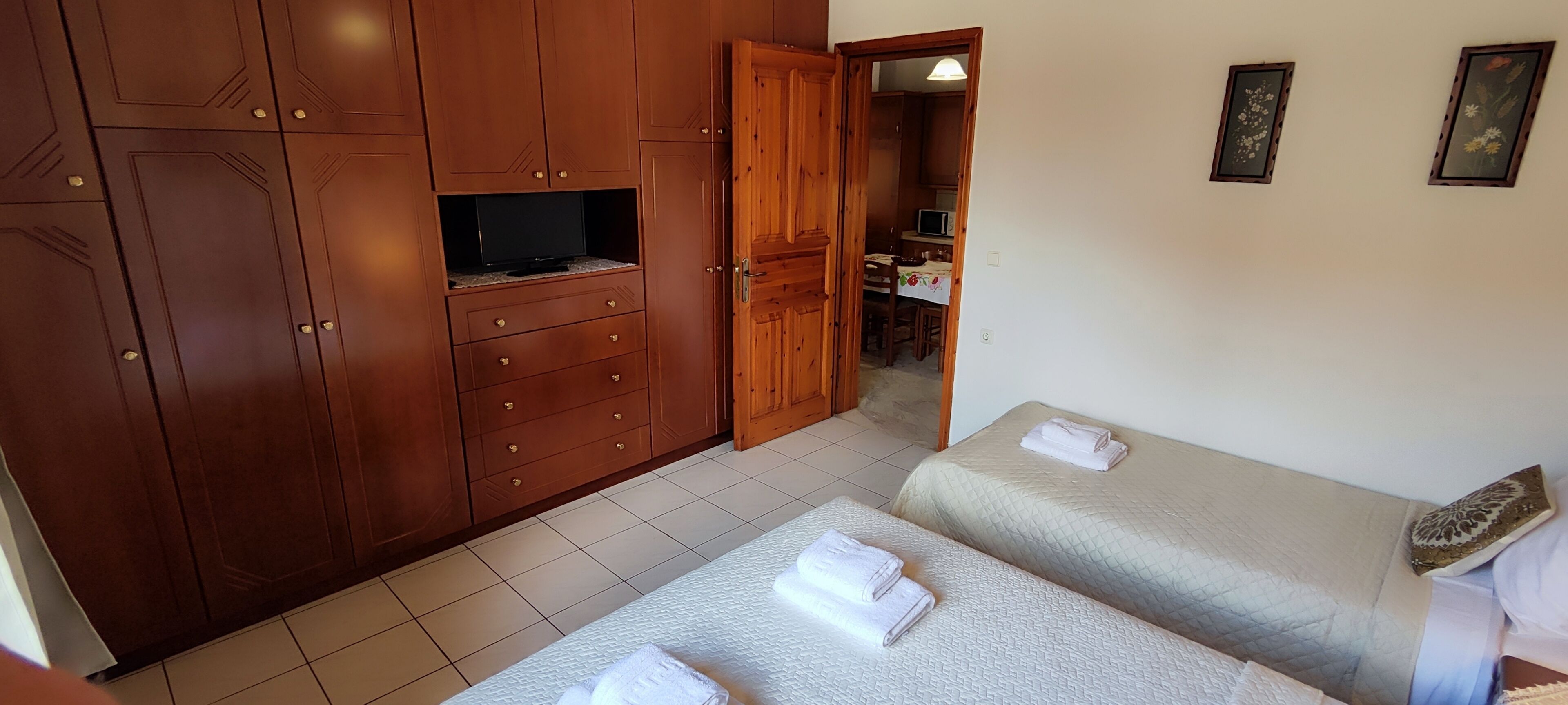 Une chambre avec deux lits, une armoire en bois, une télévision et un petit coin cuisine.