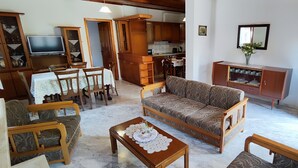 Un salon comprenant un canapé, des fauteuils, une table basse, un téléviseur et des meubles de rangement en bois.