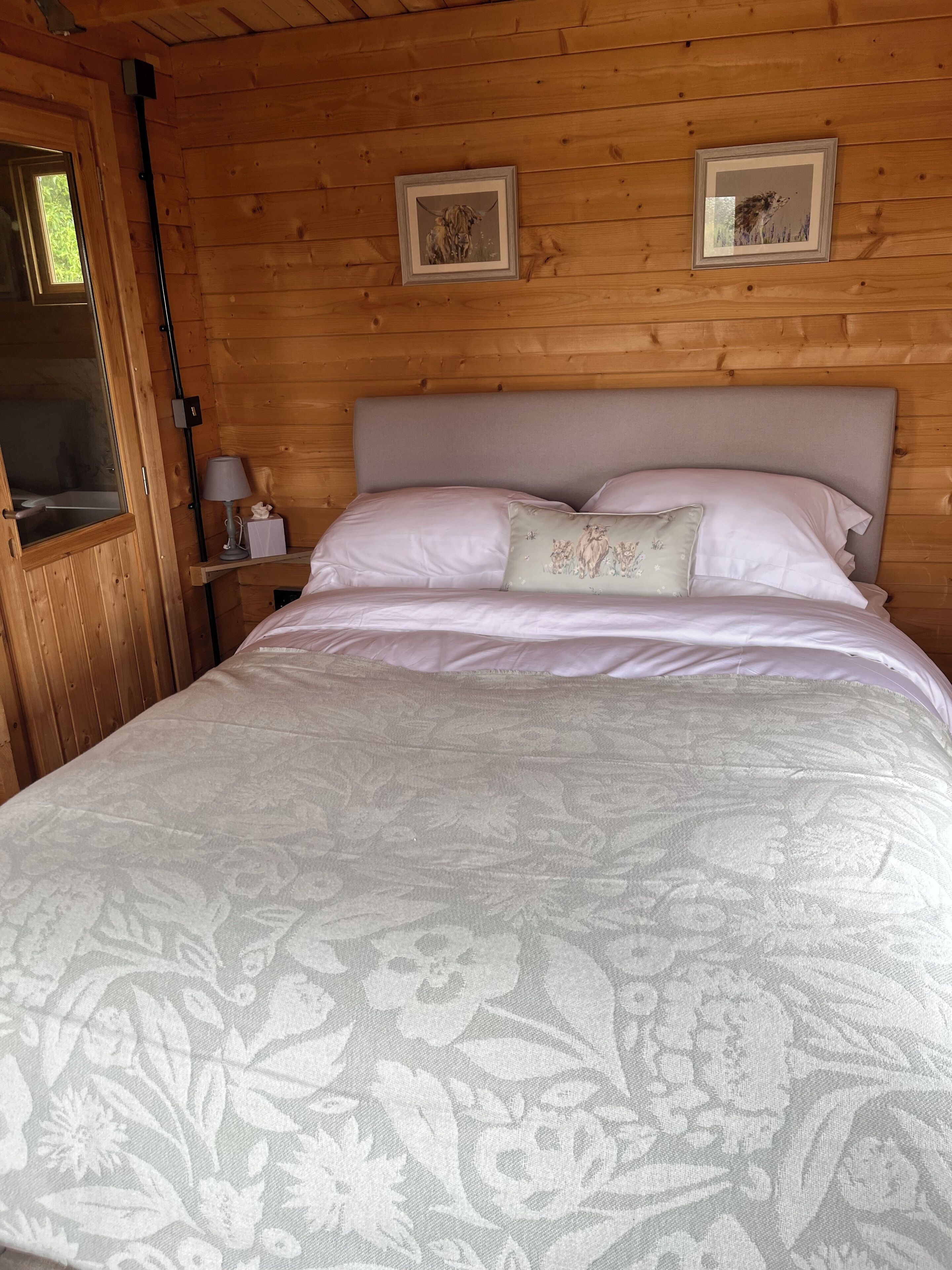 A wooden cabin bedroom with a bed, a nightstand, a lamp, and two framed pictures on the wall.