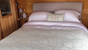 A wooden cabin bedroom with a bed, a nightstand, a lamp, and two framed pictures on the wall.