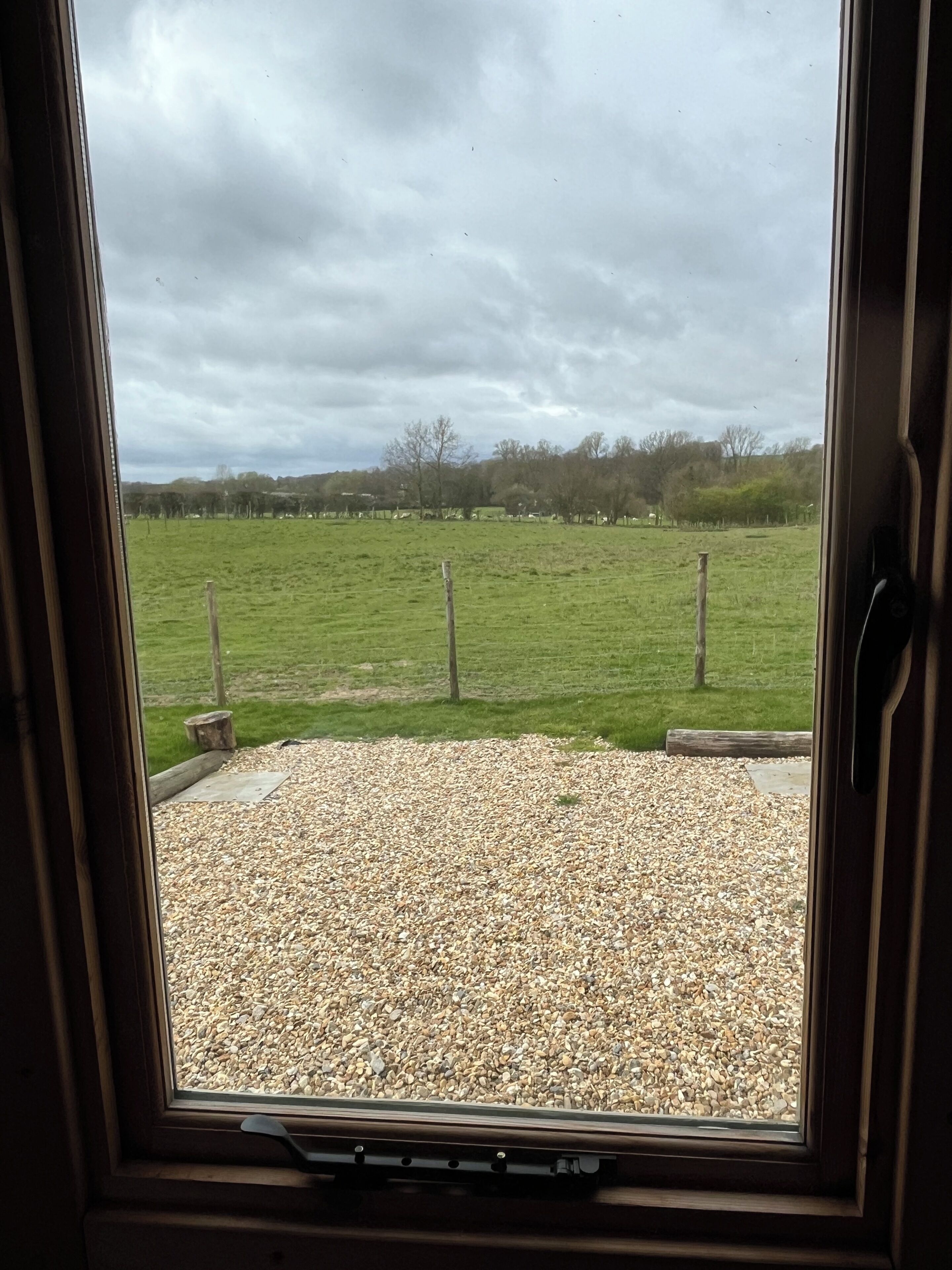 A view through a window of a gravel area with a grassy field and trees in the background.